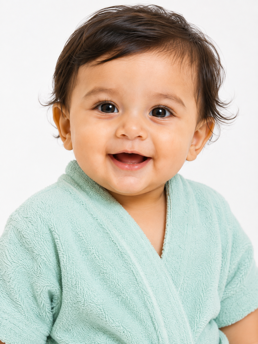 A close-up of a smiling baby wearing a soft mint green terry cloth wrap robe against a plain white background.