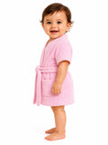 A smiling toddler standing barefoot in profile, wearing a soft pink terry cloth bathrobe with a tie belt and front patch pocket, against a plain white background.