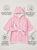 A pink baby hooded bathrobe with white trim and ear details on the hood, shown on a light beige background with feature callout icons and text for fabric, skin friendliness, washability, and suitability for infants and toddlers.