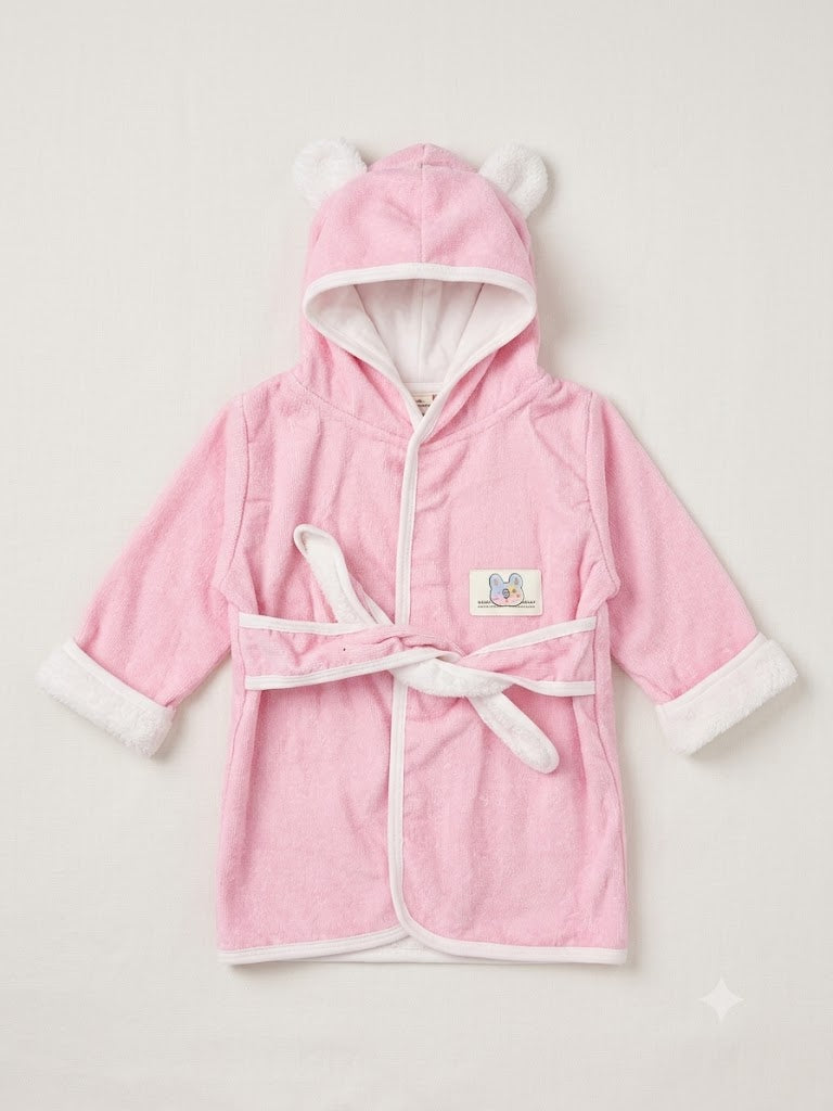 A pink hooded bathrobe with white trim, featuring plush bear ears on the hood, a white tie belt, and a small embroidered patch on the chest, displayed against a light beige background.
