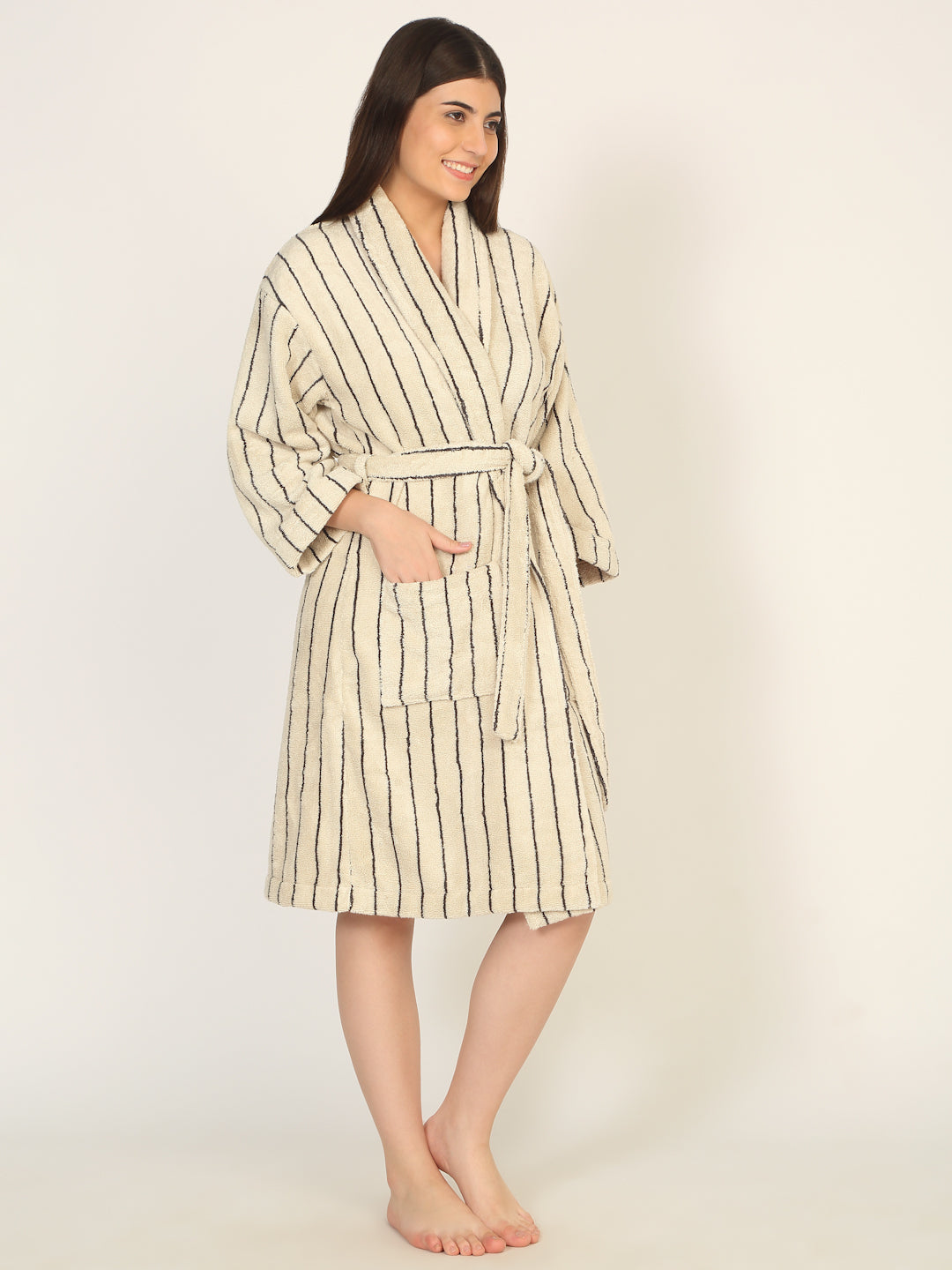 Woman wearing a striped robe holding a mug next to a wooden stool on a plain background