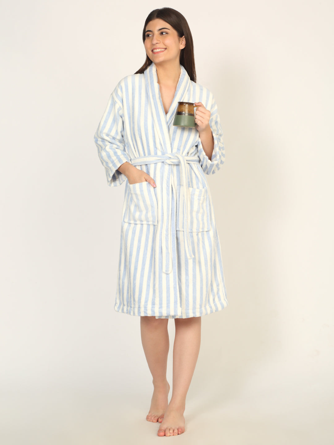 Woman wearing a striped robe holding a mug on a plain background