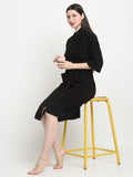 Woman sitting on a stool wearing a black micro terry bathrobe and holding a cup