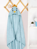 A light blue hooded towel with a cartoon bird face and small gold crown, hanging on a wooden wall rack in a bright indoor setting.