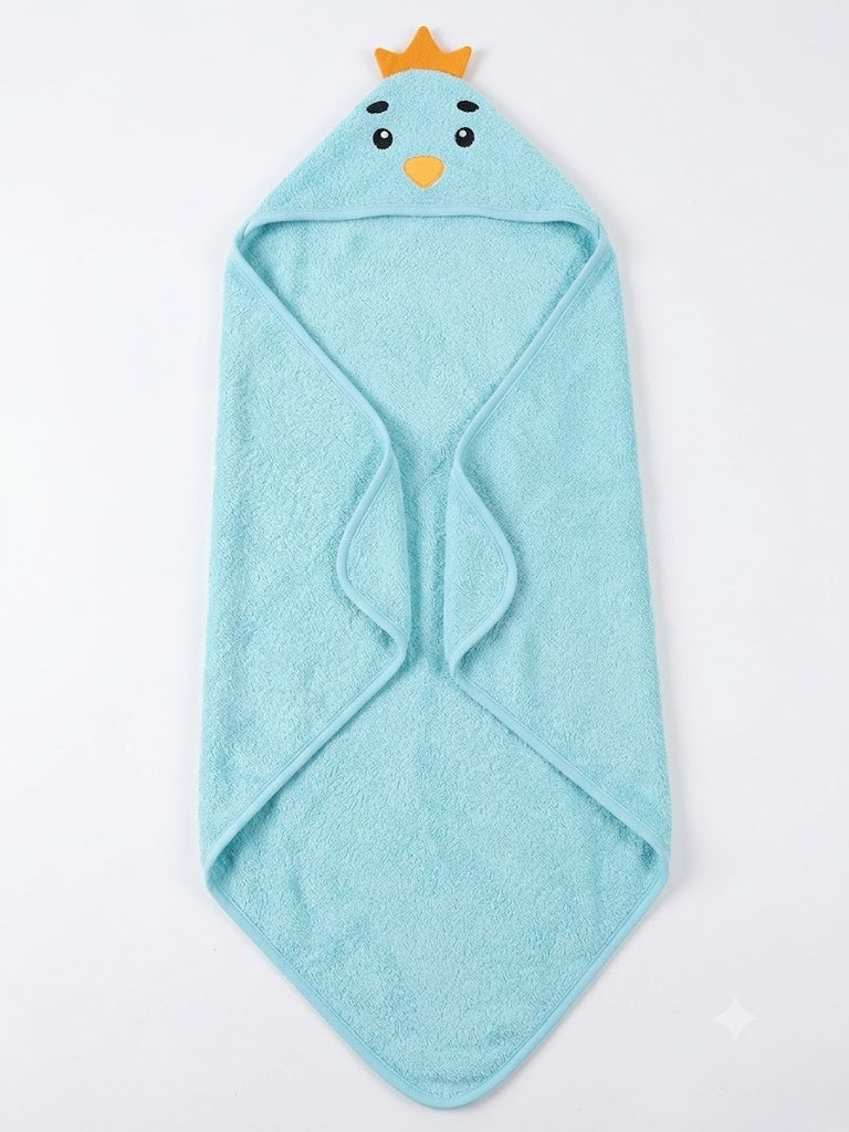 A baby crawling on a white textured blanket, wrapped in a light blue hooded towel with a cartoon bird face and small yellow crown detail.