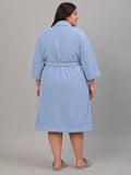 A woman wearing a light blue terry cloth bathrobe, shown from the back against a solid gray studio background.