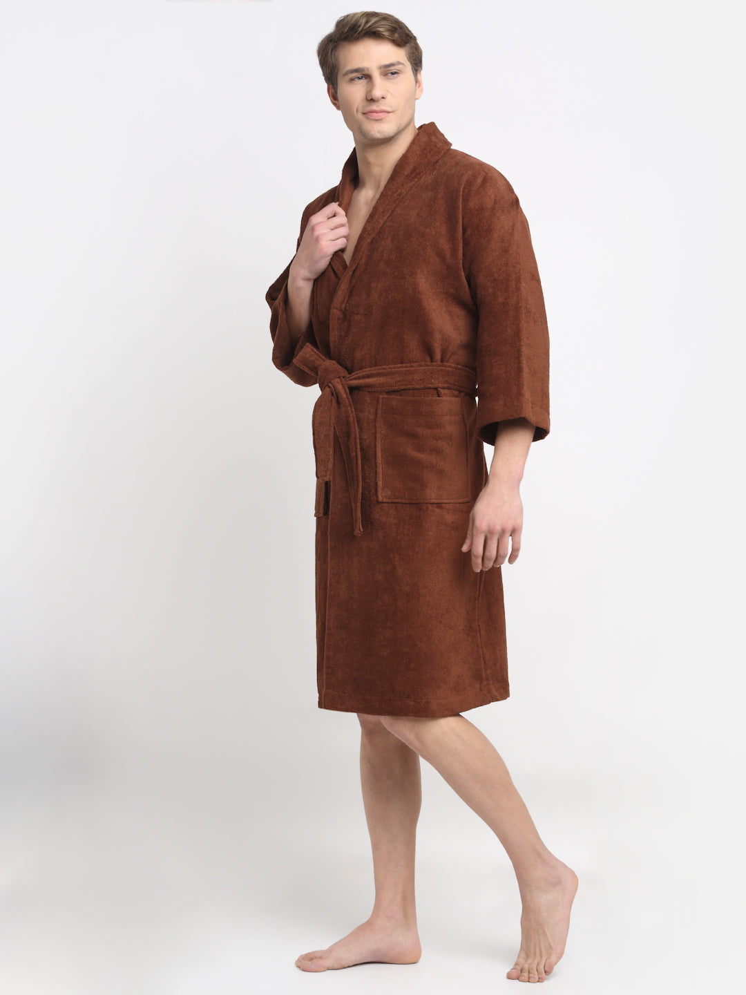 A person standing in a relaxed pose wearing a brown, long-sleeved, unisex cotton bathrobe that reaches up to the knees.
