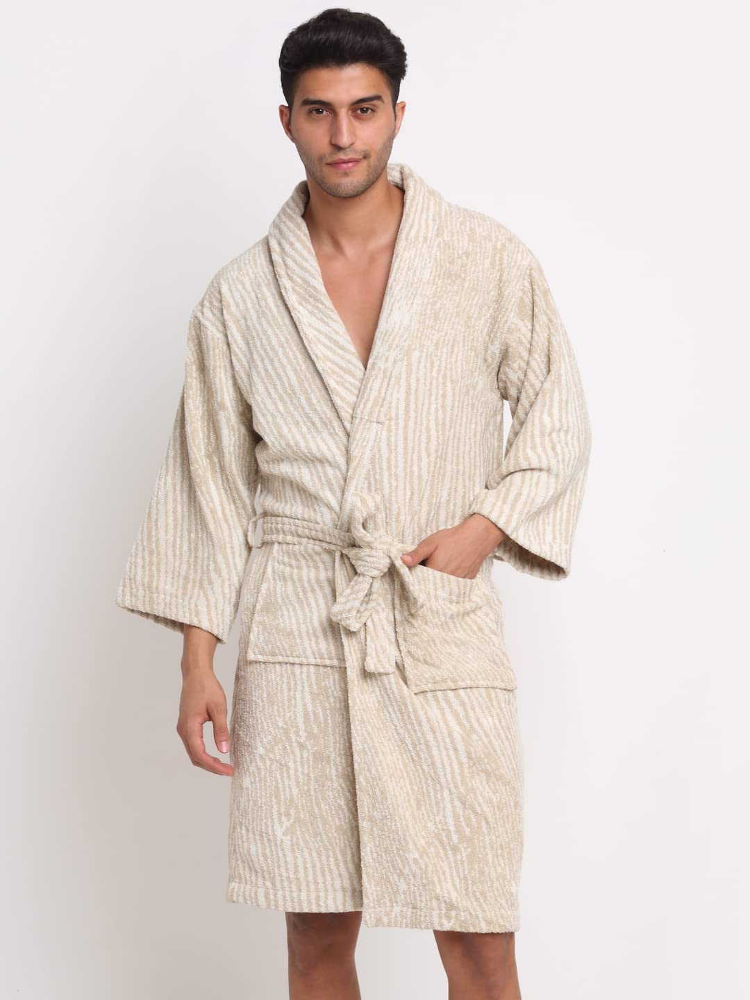 A man wearing a textured cream and beige vertically striped bathrobe with a tie waist and front pockets, standing against a plain white studio background.