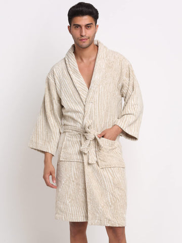 A man wearing a textured cream and beige vertically striped bathrobe with a tie waist and front pockets, standing against a plain white studio background.
