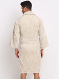 A man viewed from the back wearing a cream and beige vertically striped bathrobe against a plain white studio background.
