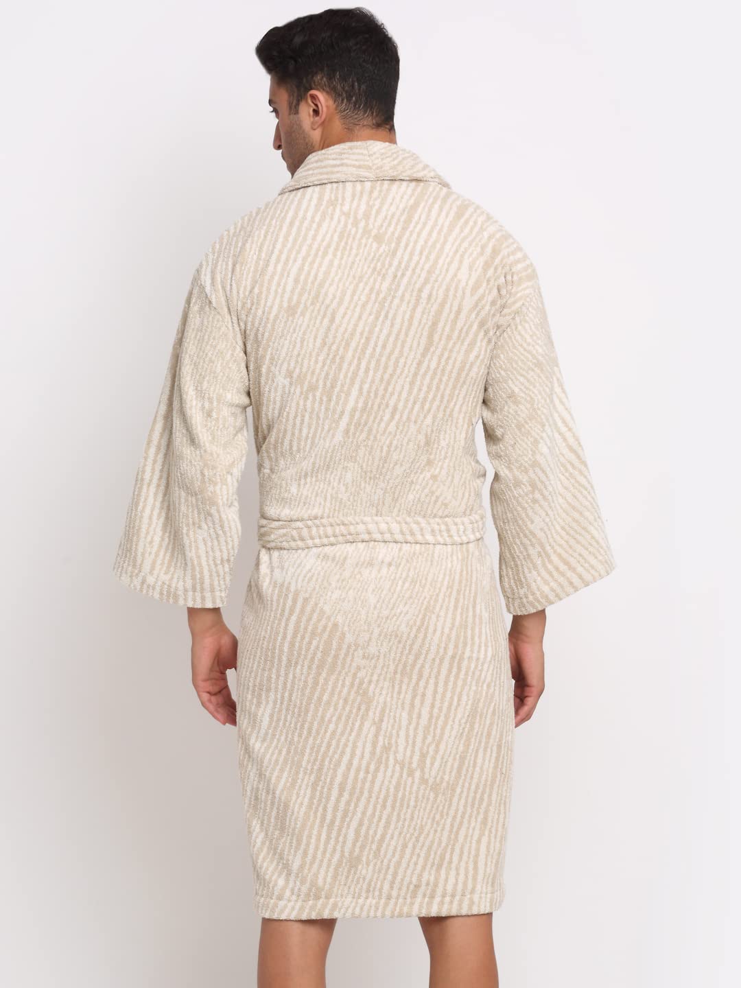 A man viewed from the back wearing a cream and beige vertically striped bathrobe against a plain white studio background.