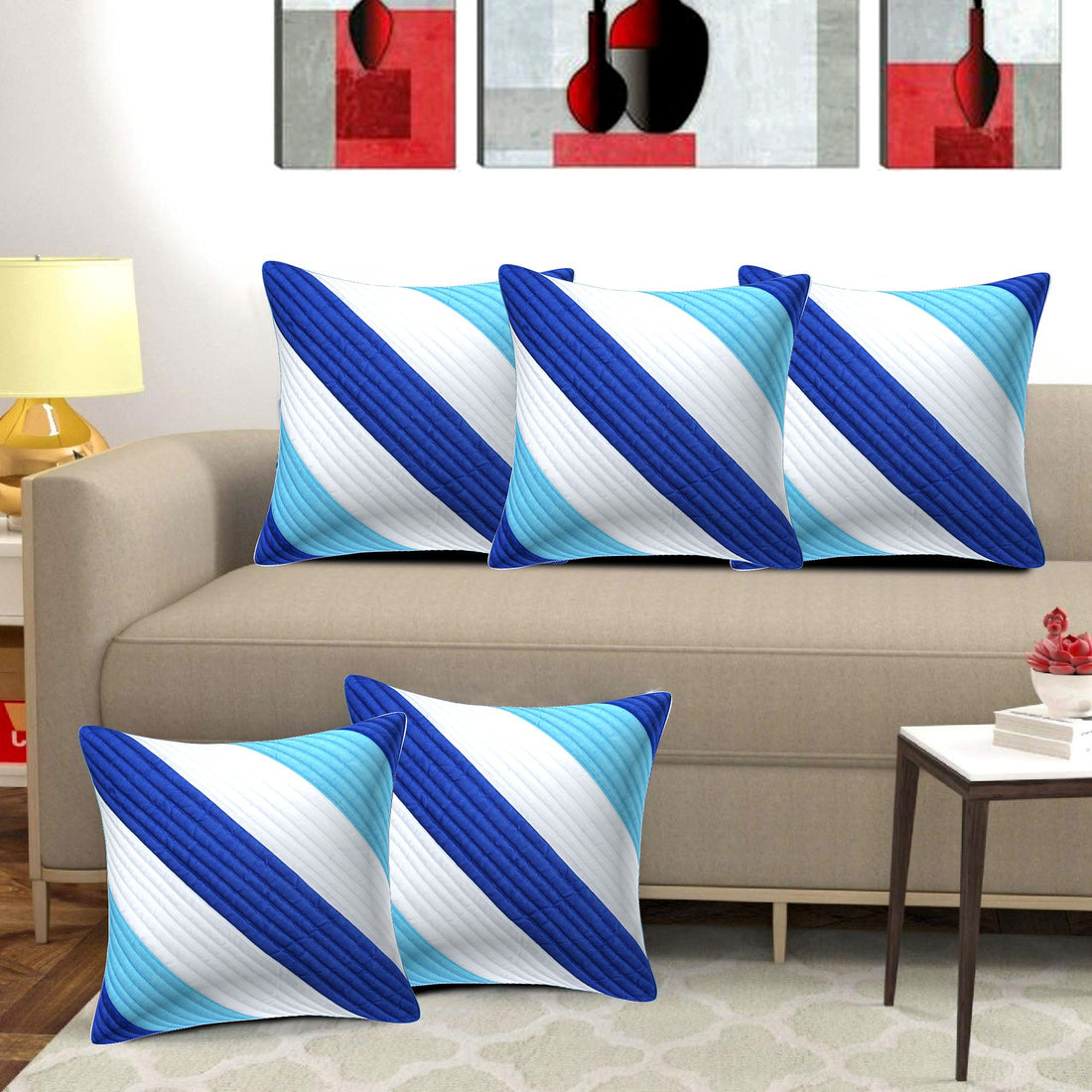 Set of blue and white striped pillows on a beige sofa with abstract art in the background.