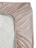 A close-up of a fitted sheet with gathered elastic edges, shown partially pulled over a mattress. The sheet is a dusty blush pink color, and the mattress underneath is light gray.