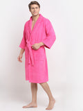 A person standing in a relaxed pose wearing a fuchsia, long-sleeved, unisex cotton bathrobe that reaches up to the knees.