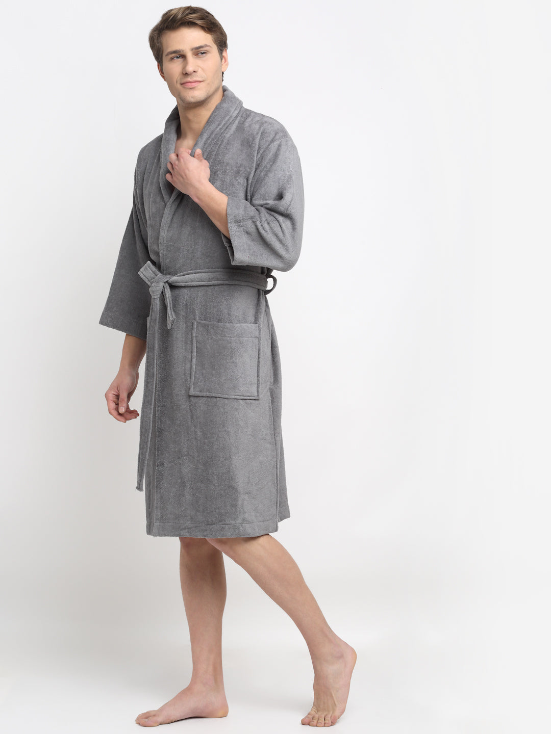 A person standing and smiling, wearing a grey 100% cotton unisex bathrobe with a belt tied around the waist.