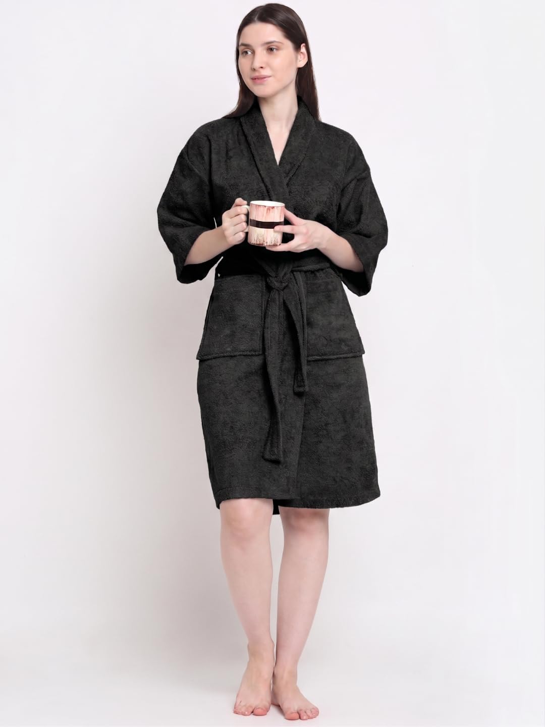 A woman modeling a black textured bathrobe with a tie belt and front pockets, standing against a plain white background.