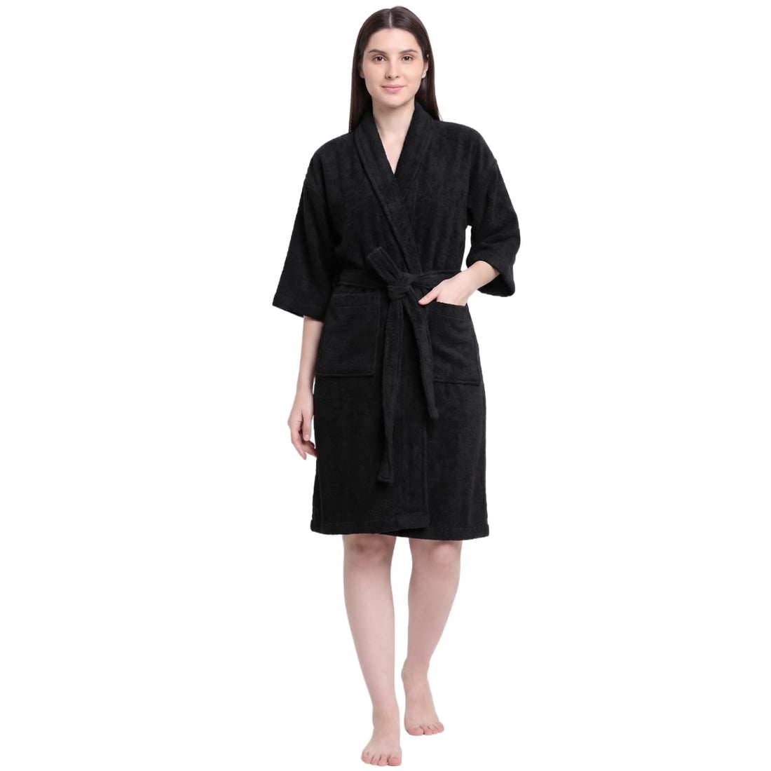A woman modeling a black textured bathrobe with a tie belt and front pockets, standing against a plain white background.
