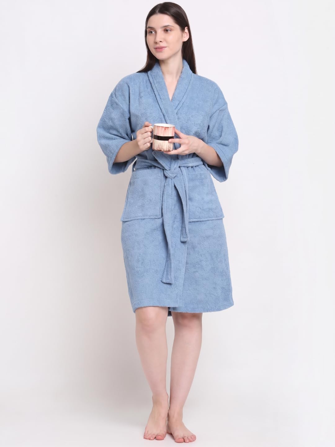 A woman modeling a light blue textured bathrobe with a tie waist and front pockets, standing against a plain white background.