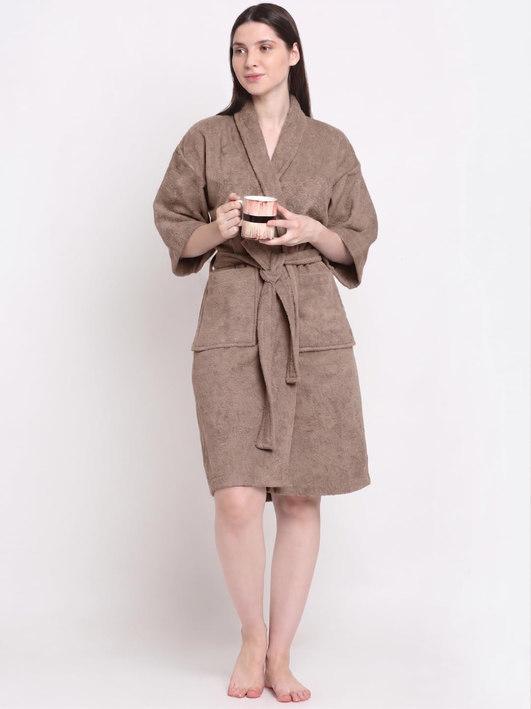 A woman modeling a brown bathrobe with a tie belt and front pockets, standing against a plain white background.