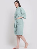 A woman modeling a light mint green bathrobe with wide sleeves and a tie waist, standing against a plain light gray studio background.