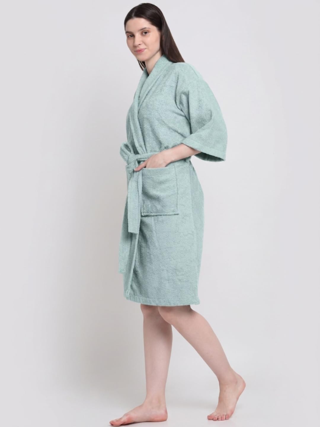 A woman modeling a light mint green bathrobe with wide sleeves and a tie waist, standing against a plain light gray studio background.
