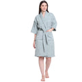 A woman modeling a light sage green bathrobe with three-quarter sleeves, a matching tie belt, and front patch pockets, set against a plain white background.
