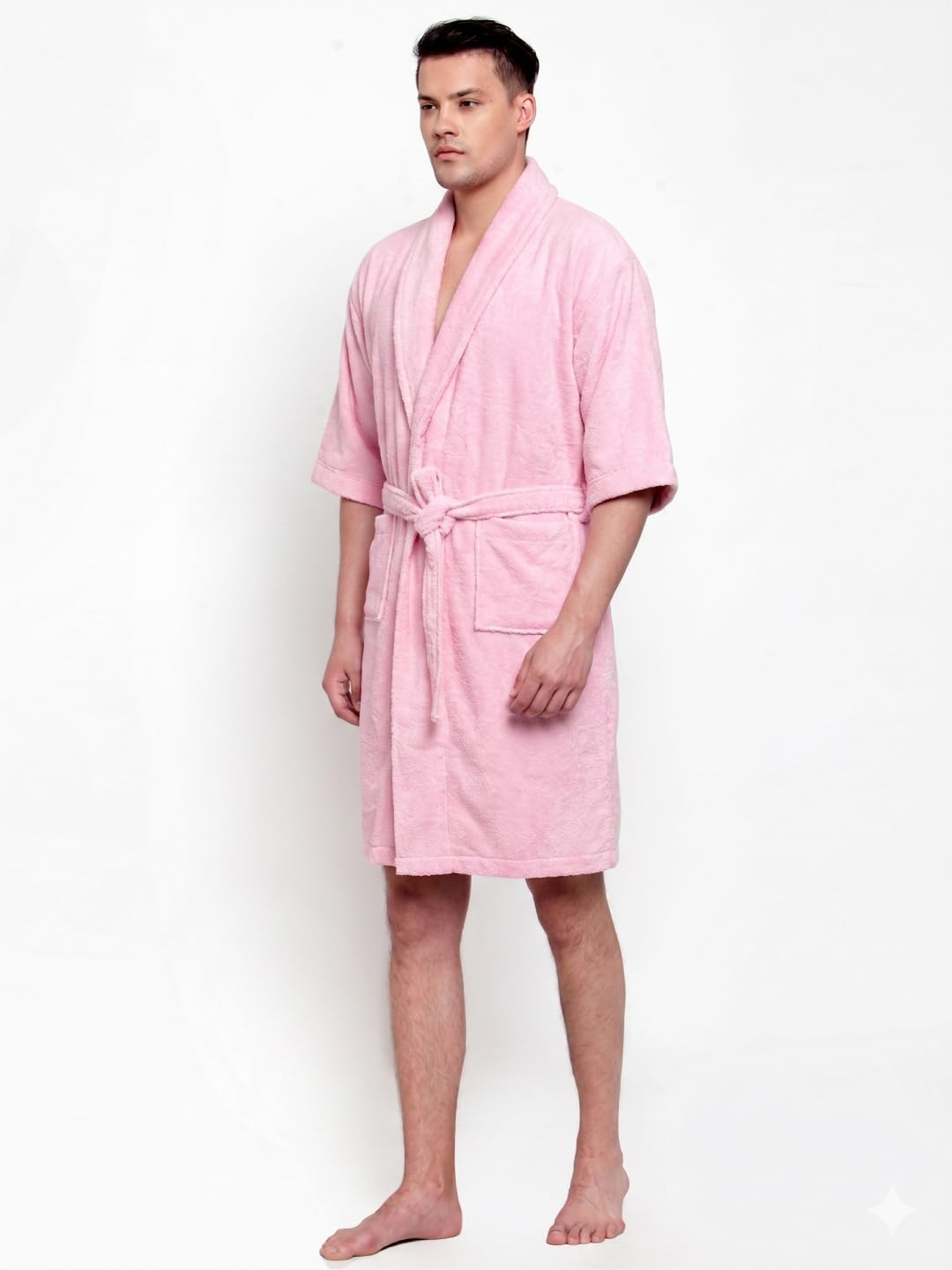 A man modeling a light pink terry cloth bathrobe with a tie belt, standing against a plain white studio background.