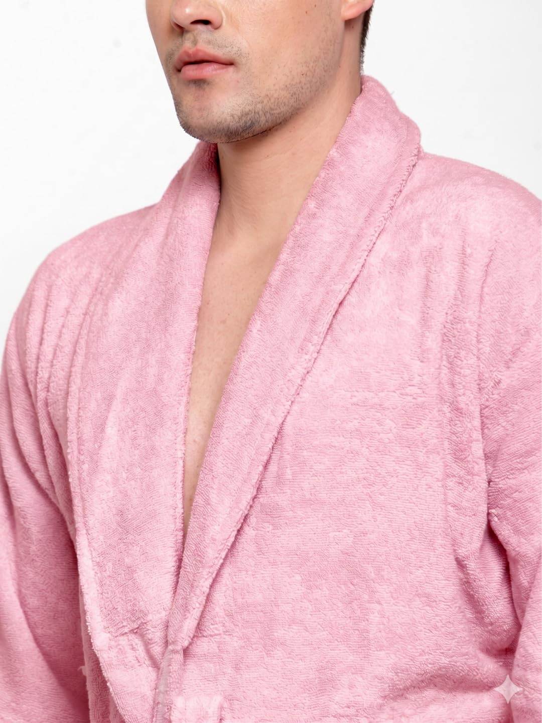 A man modeling a light pink terry cloth bathrobe with a tie belt, standing against a plain white studio background.