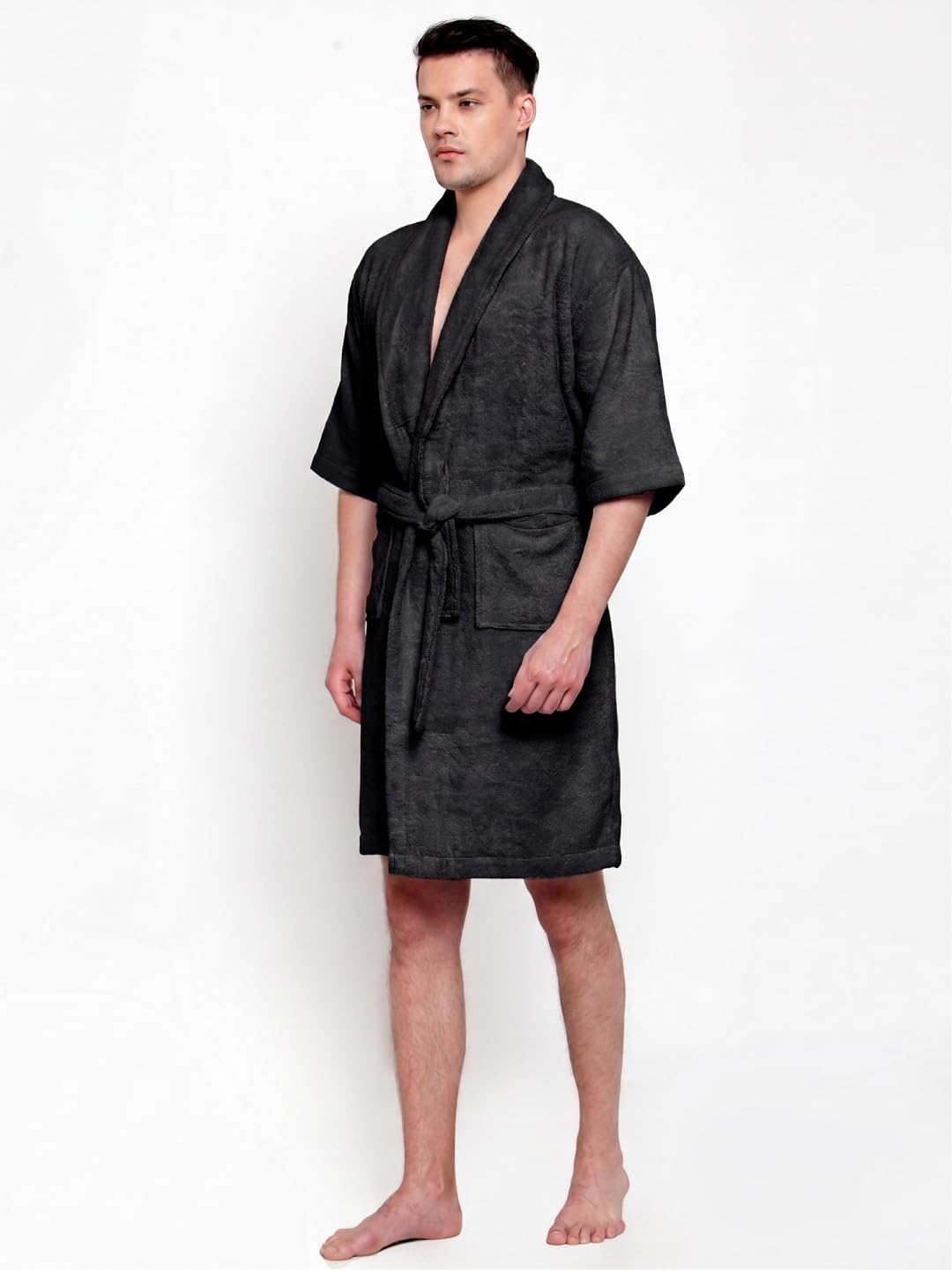 A man modeling a black textured bathrobe with a shawl collar, waist tie, and front pockets against a plain white background.