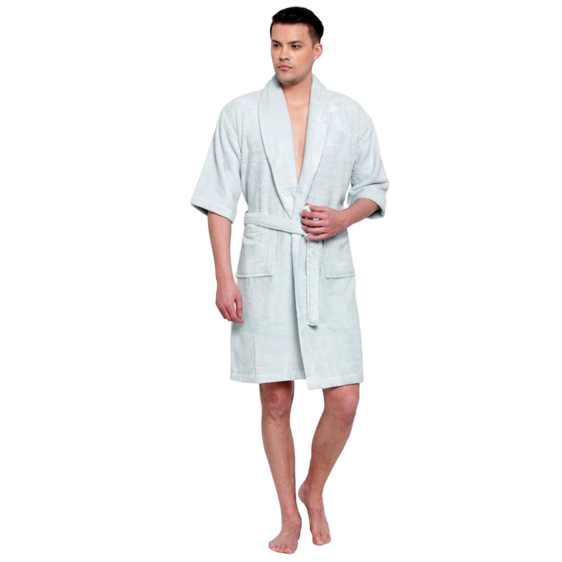 A man modeling a light sage green terry cloth bathrobe with a tie belt and front pockets, standing against a plain white background.