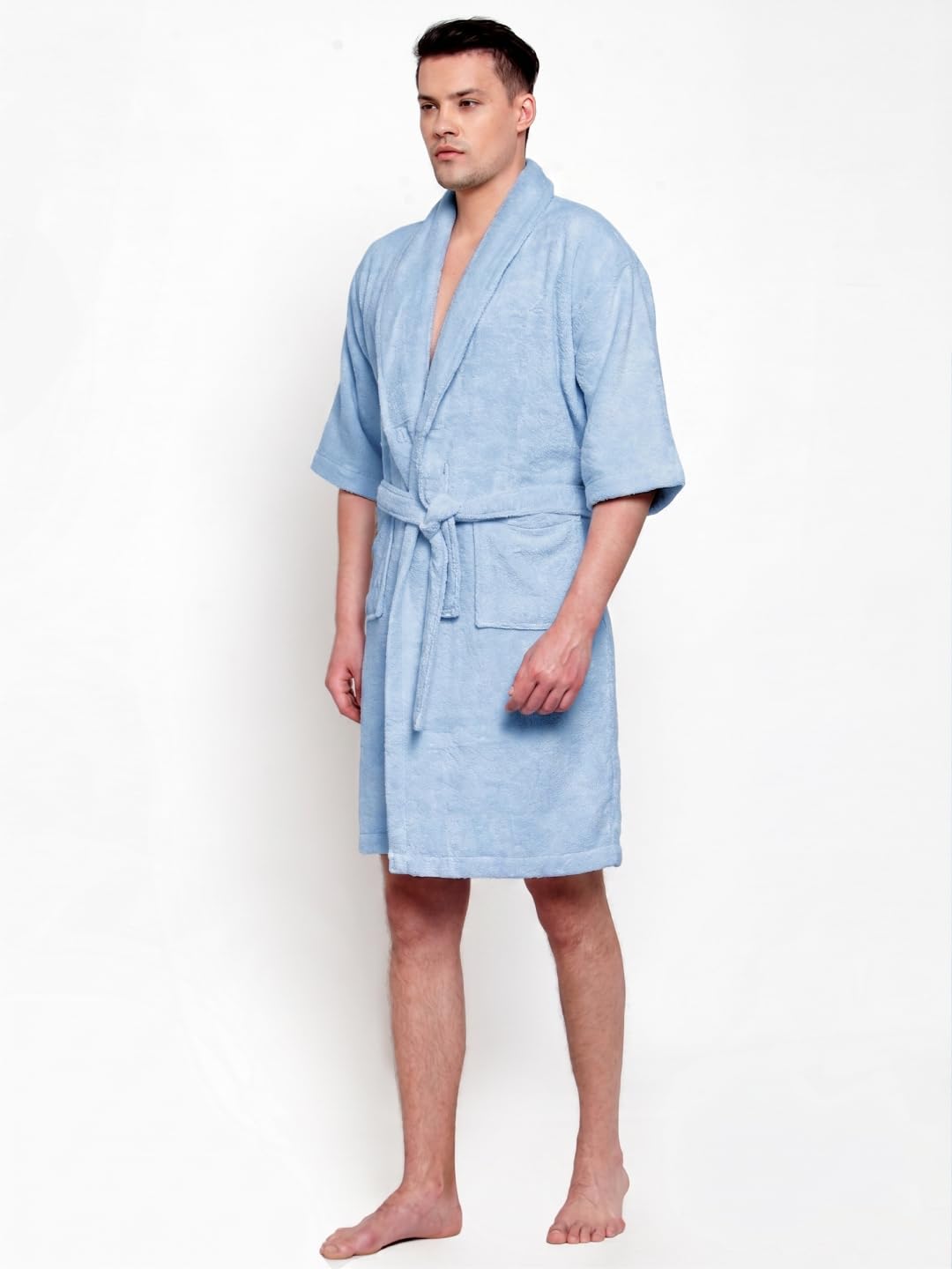 A man modeling a light blue terry cloth bathrobe with a shawl collar, waist tie, and front patch pockets against a plain white background.