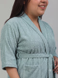 A person wearing a plush, light blue-green terry cloth bathrobe with a tie waist and front pocket, shown in a close-up shot against a neutral gray background.