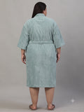 A person shown from the back wearing a light sage green bathrobe against a plain gray studio background.