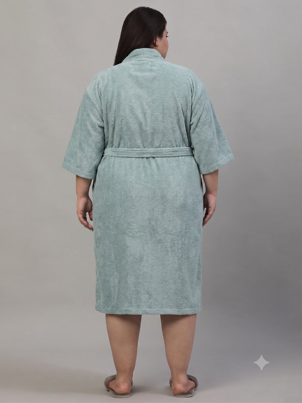 A person shown from the back wearing a light sage green bathrobe against a plain gray studio background.