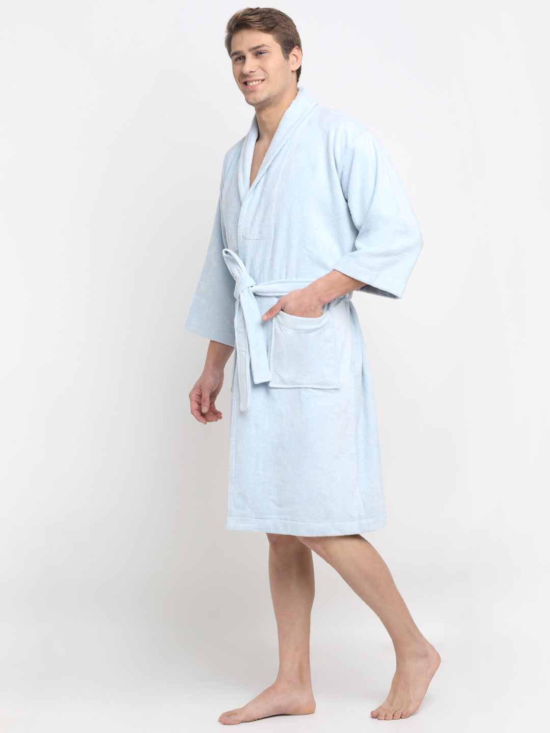 A person standing and smiling, wearing a light blue 100% cotton unisex bathrobe with a belt tied around the waist.