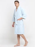 A person standing in a relaxed pose wearing a Light Blue, long-sleeved, unisex cotton bathrobe that reaches up to the knees.