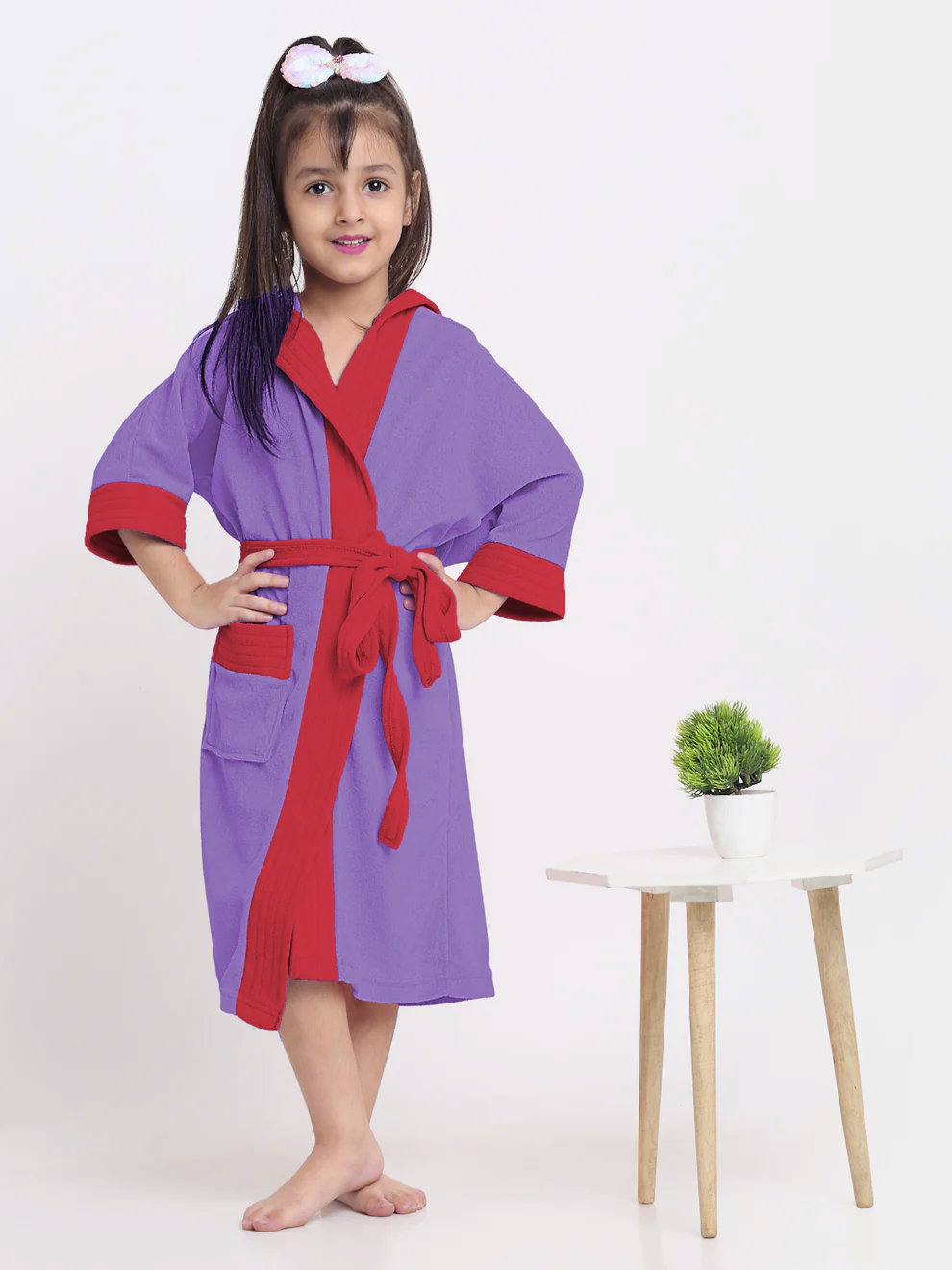 Child wearing an indigo and red robe with a small plant on a white table in the background