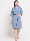 A woman standing and modeling an ocean blue 100% cotton unisex bathrobe with a belt tied around the waist.