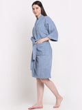 A Woman and wearing a ocean blue 100% cotton bathrobe with a waist belt and front pockets.