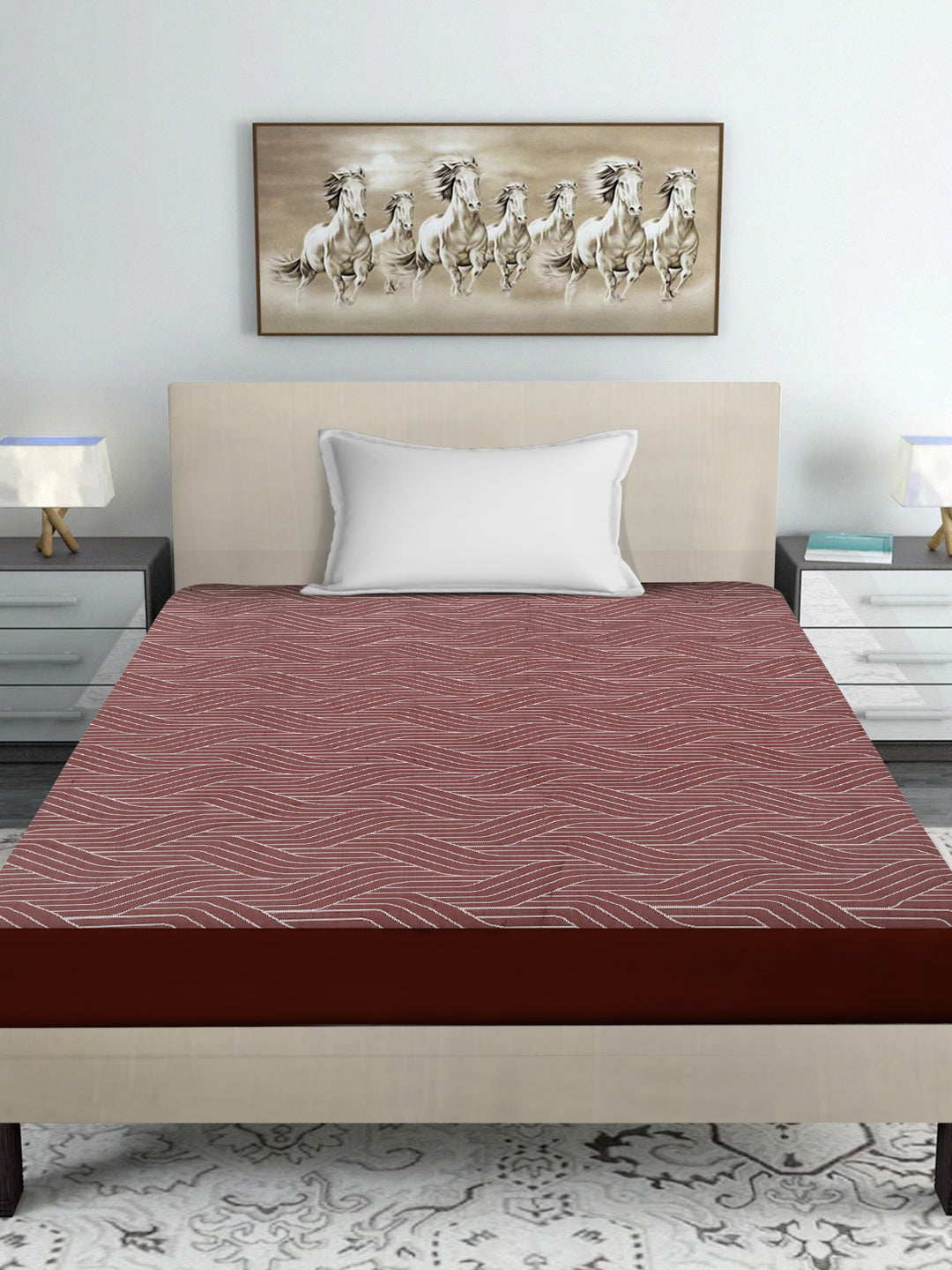 Bed with a red and brown fitted sheet in a room with a white wall and plants.