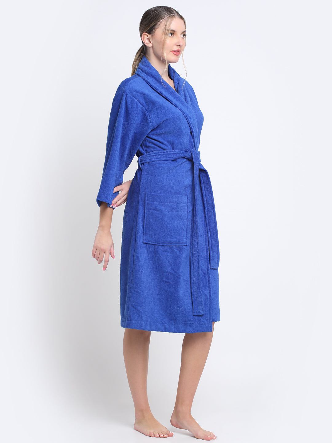 A woman is wearing a royal blue 100% cotton bathrobe with a waist belt and front pockets.