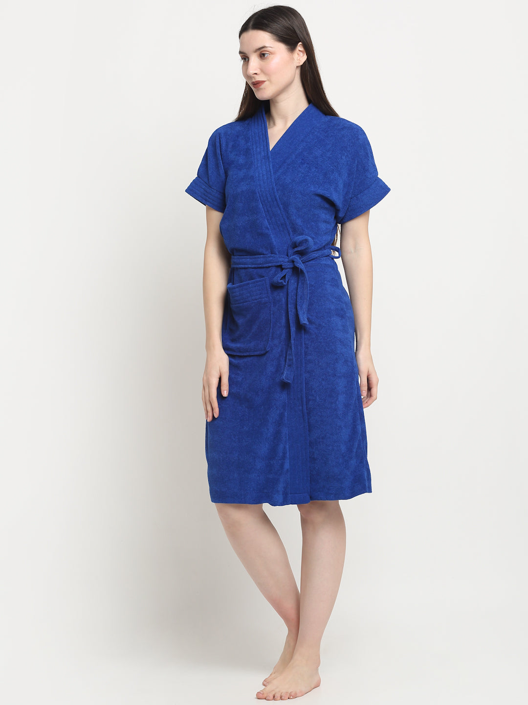 A woman standing, wearing a soft royal blue terry bathrobe with a V-neck and a tie belt.