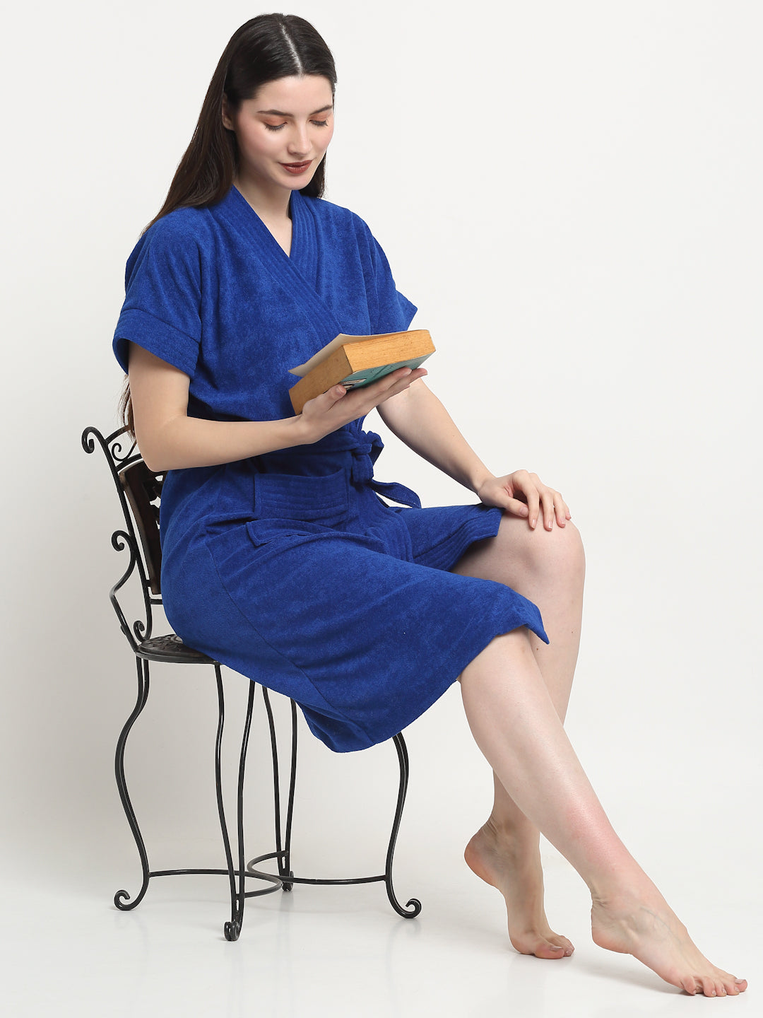 A woman sitting on a chair and wearing a royal blue micro terry bathrobe and holding a book