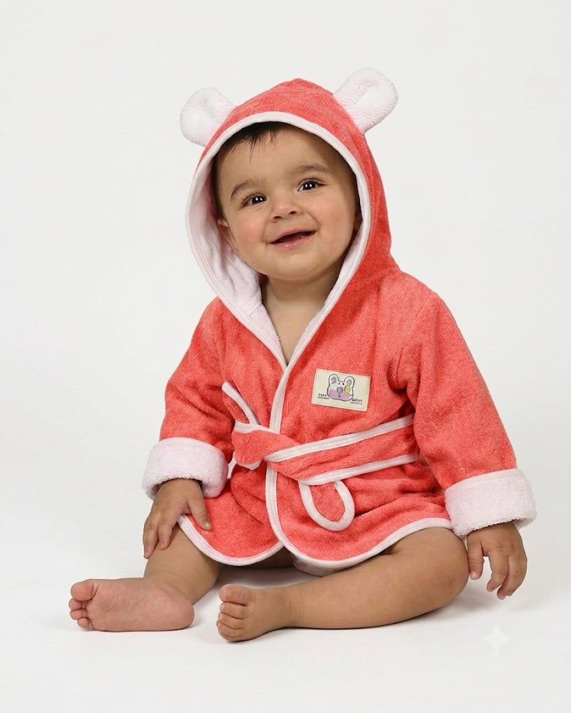 A baby wearing a coral Red hooded bathrobe with white trim and bear ears on the hood, sitting against a plain white background.