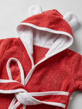 A red hooded bathrobe made of soft terry cloth, featuring white trim, a matching white tie belt, and plush white bear ears on the hood, shown against a light gray background.