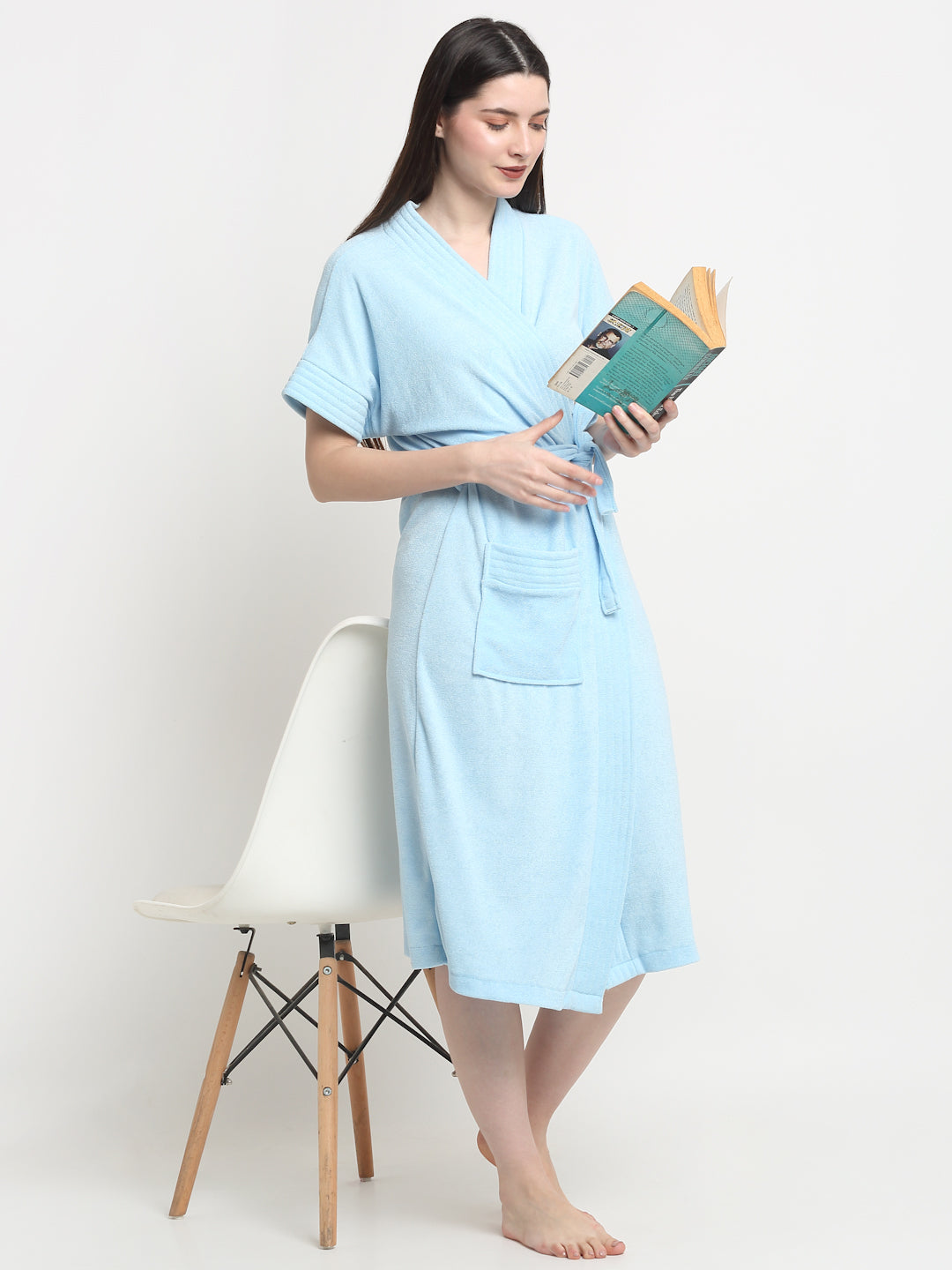 A woman standing beside a chair wearing a sky-blue micro terry bathrobe and holding a book