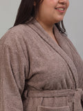 A close-up of a person wearing a plush, taupe-brown terry cloth bathrobe against a solid light gray background.