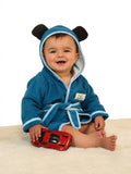 A baby wearing a blue plush hooded bathrobe with black bear ears and white trim, sitting on a cream rug and holding a red toy car.