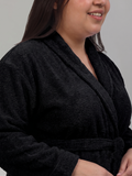 A close-up of a person wearing a plush black bathrobe against a plain light gray background.