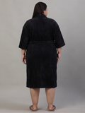 A person shown from the back wearing a black bathrobe with three-quarter sleeves and a tie belt, standing against a plain light gray studio background.